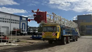 Large yellow truck with industrial equipment parked outside warehouse buildings.