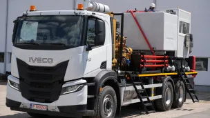 White Iveco utility truck with equipment and hoses parked outside a building.