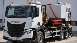 White utility truck with red and black equipment parked by a building.