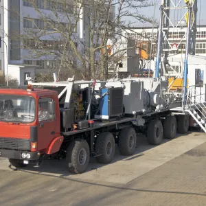Large red and black mobile drilling truck parked near industrial buildings.