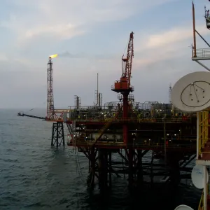 Offshore oil rig with cranes and gas flare at sunset over the ocean.