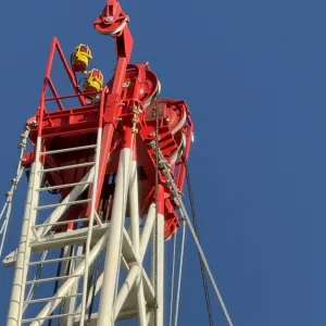 Red and white oil rig tower structure against a clear blue sky.