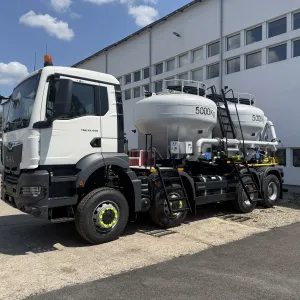 White industrial truck with large tanks parked beside a building on a sunny day.