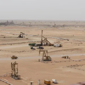 Several oil pumps operating in a vast, sandy desert landscape under a hazy sky.